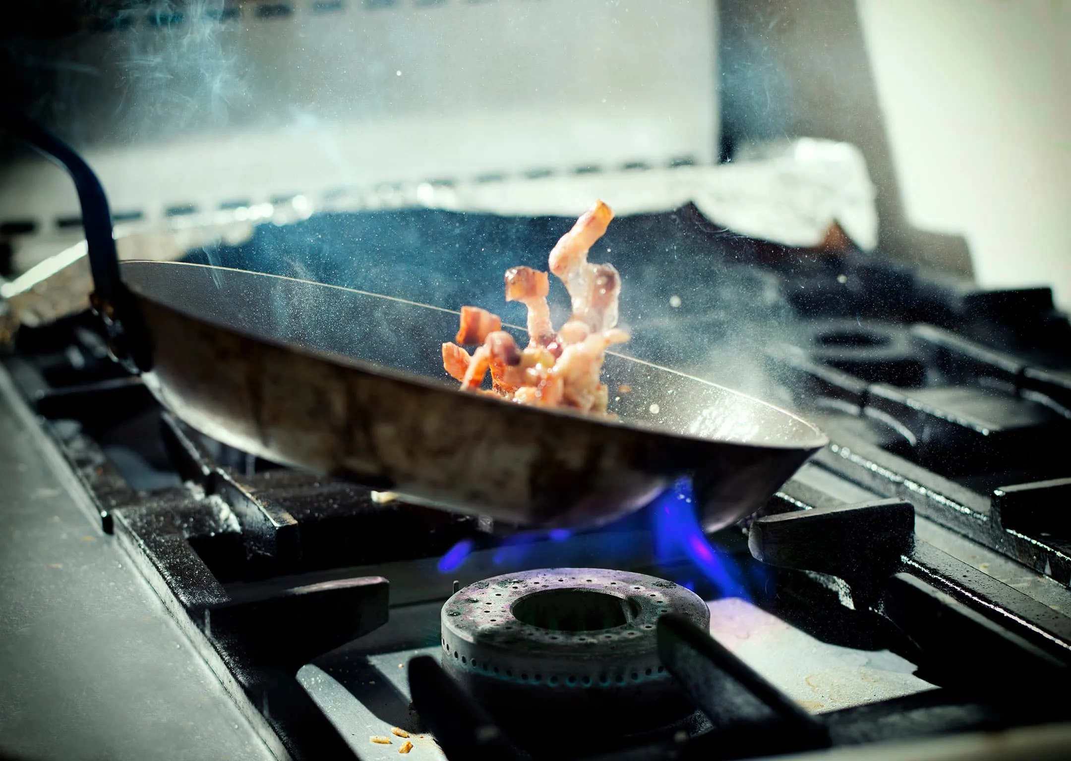 A frying pan tossing shrimp over a blue flame