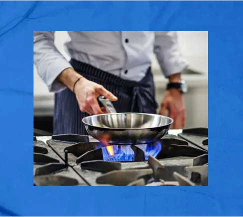 A chef cooking on a skillet with a gas flame coming from the stove